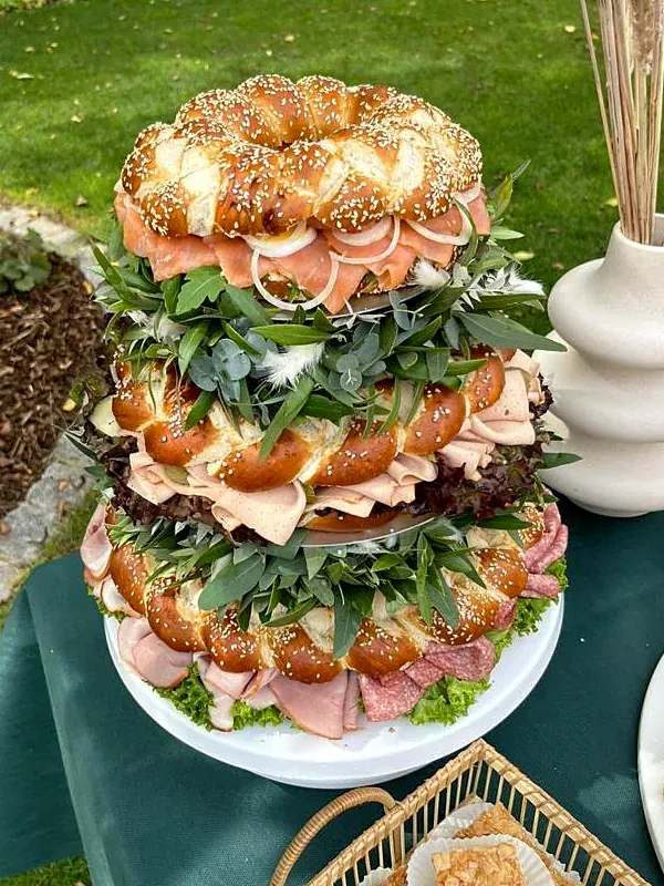 Drei gestapelte Laugenringe mit Lachs, Schinken und Salami, dekoriert mit Eukalyptus, auf einem Buffet im Garten
