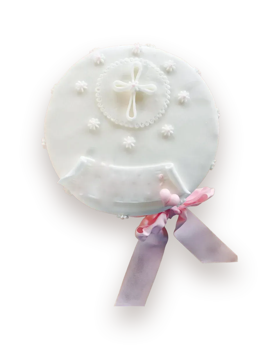 Runde weiße Fondanttorte mit einem Kreuz aus Zuckerguss im Perlenkranz, kleinen weißen Blüten, Zuckerband und rosa Schleife