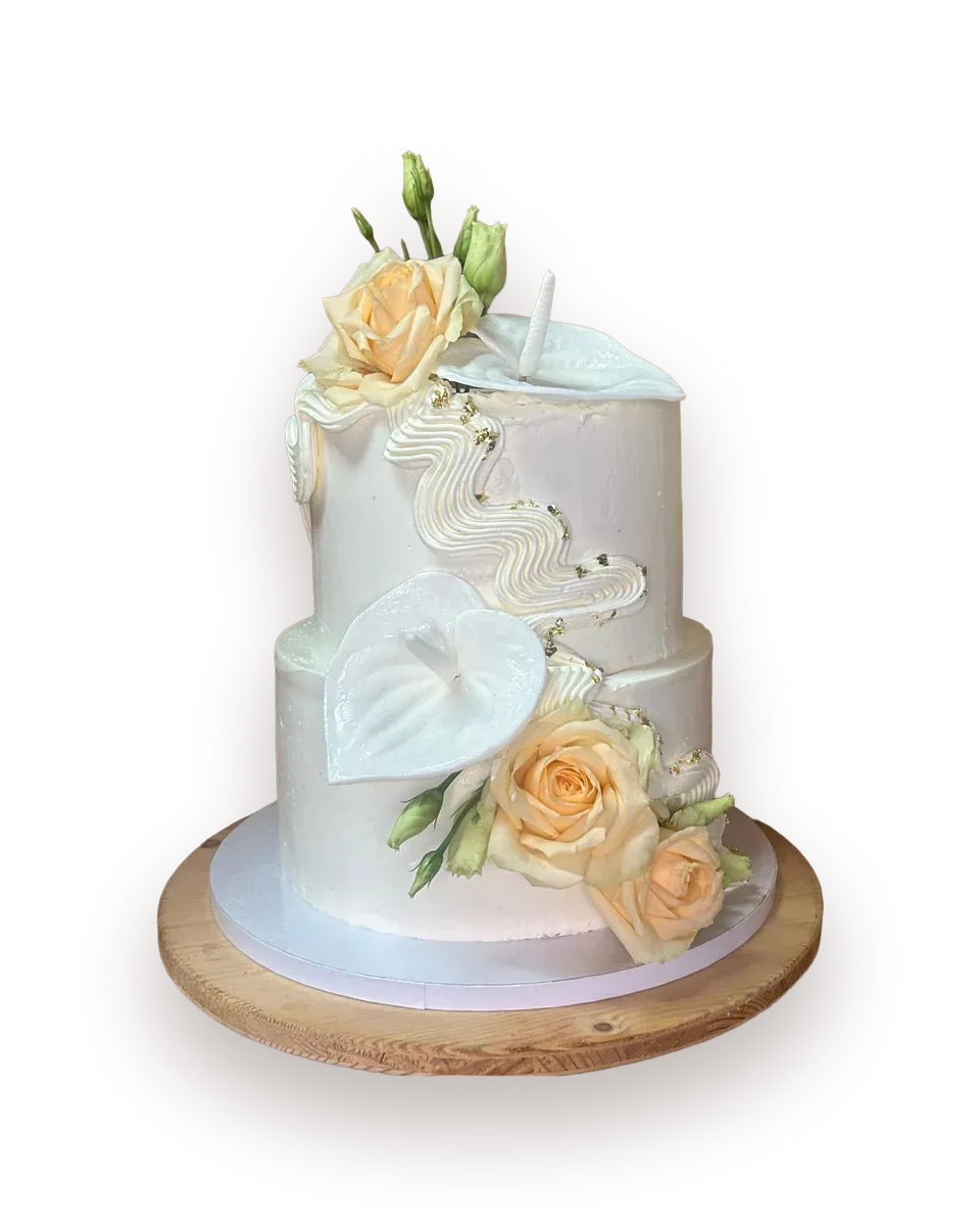 Zweistöckige weiße Hochzeitstorte mit weißer Anthurie, cremefarbenen Rosen und geschwungener Zuckerapplikation, auf einer Holzplatte