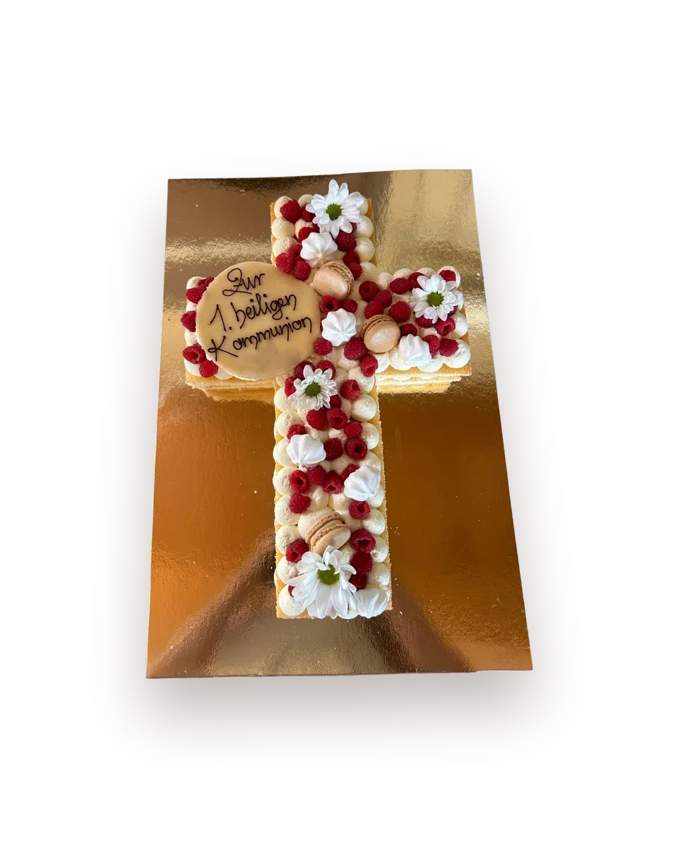 Kreuzförmige Torte mit Himbeeren, Sahne- und Baisertupfen, Macarons und weißen Margeriten, dazu eine Marzipanscheibe mit der Aufschrift „Zur 1. heiligen Kommunion"