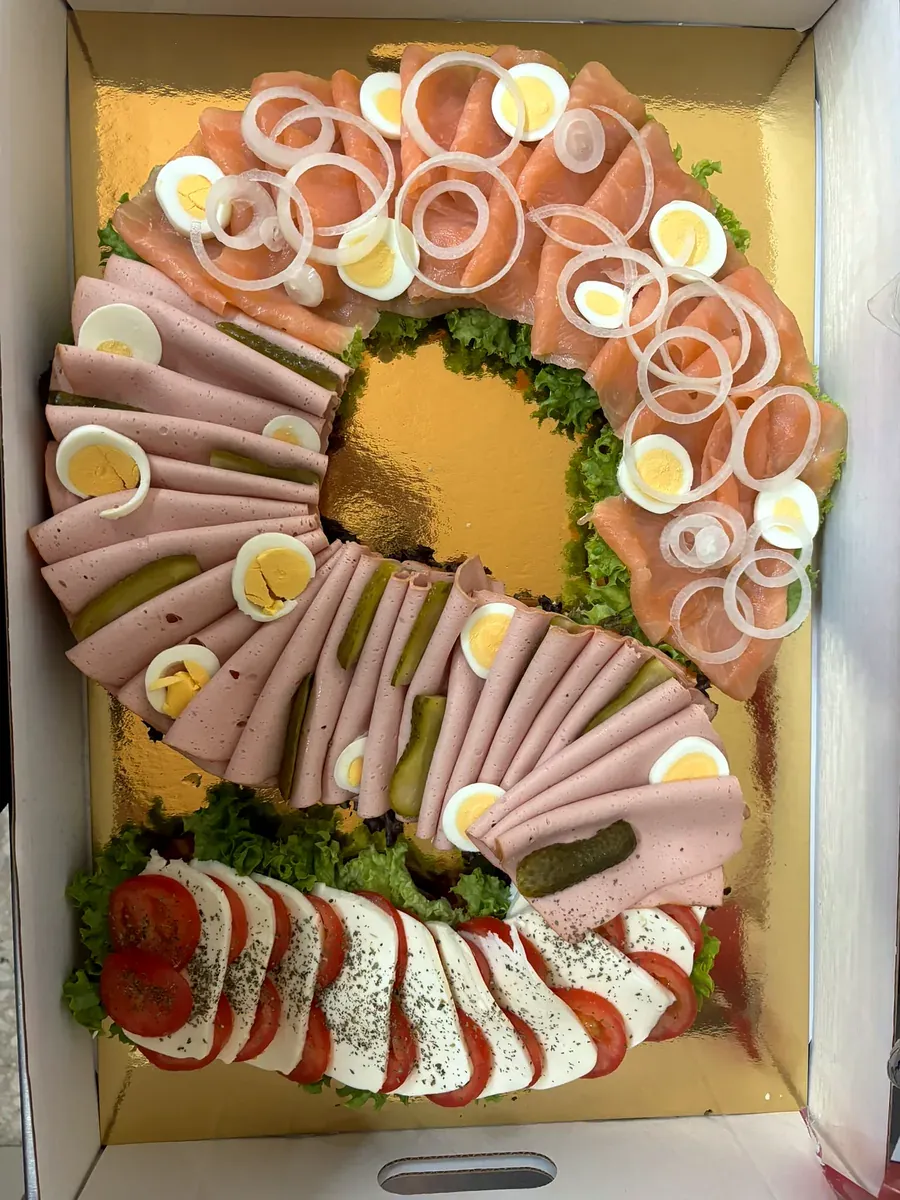 Herzhafte Zahlentorte in Form einer Sechs, geöffnet: Räucherlachs mit Zwiebelringen und Ei, Fleischwurst mit Gurke, Tomate-Mozzarella auf Salat