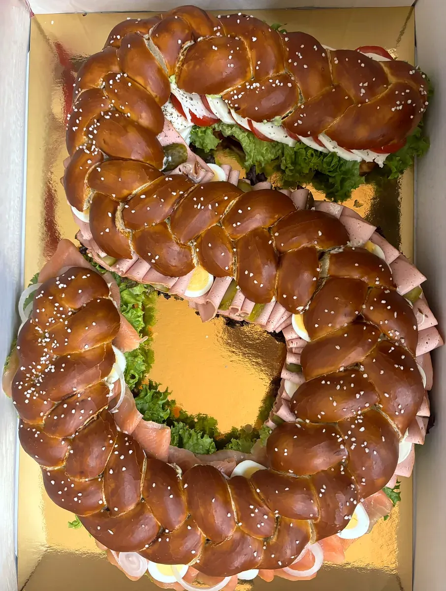 Herzhafte Zahlentorte in Form einer Sechs aus geflochtenem Laugenzopf, belegt mit Lachs, Wurst und Tomate-Mozzarella, auf Goldpappe im Karton
